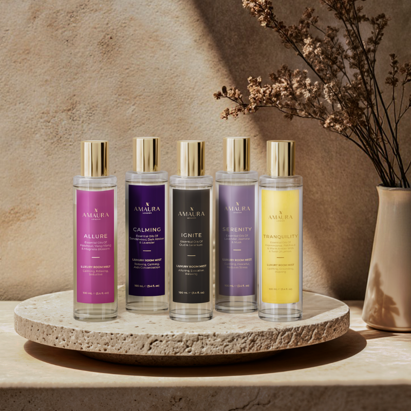 Set of room mist bottles on a stone tray with a vase of dried flowers against a beige wall.